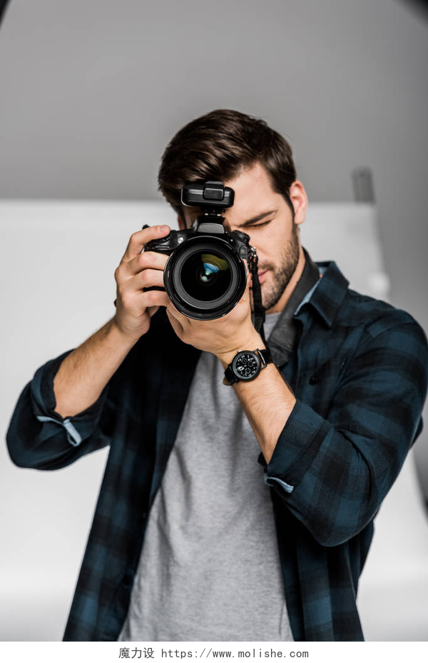 英俊的年轻男性摄影师正在用相机拍摄英俊的年轻男性摄影师使用专业相机在照相馆